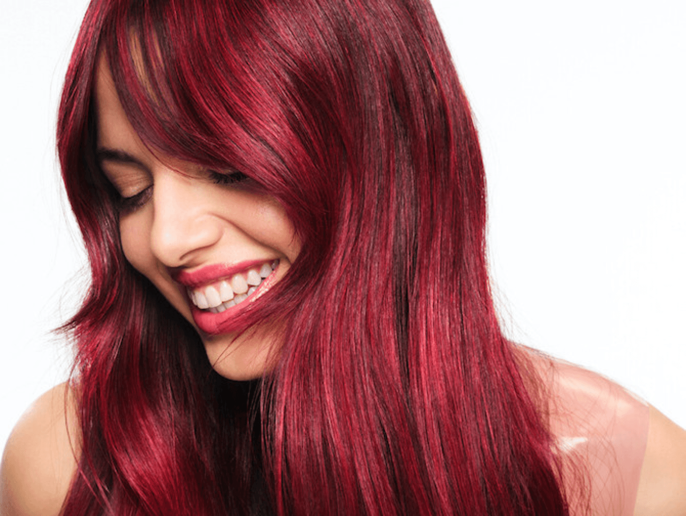 Smiling woman with long, glossy red hair featuring a seamless colour melt from deep burgundy roots to vibrant ruby tones, showcasing a professional hair colour result.