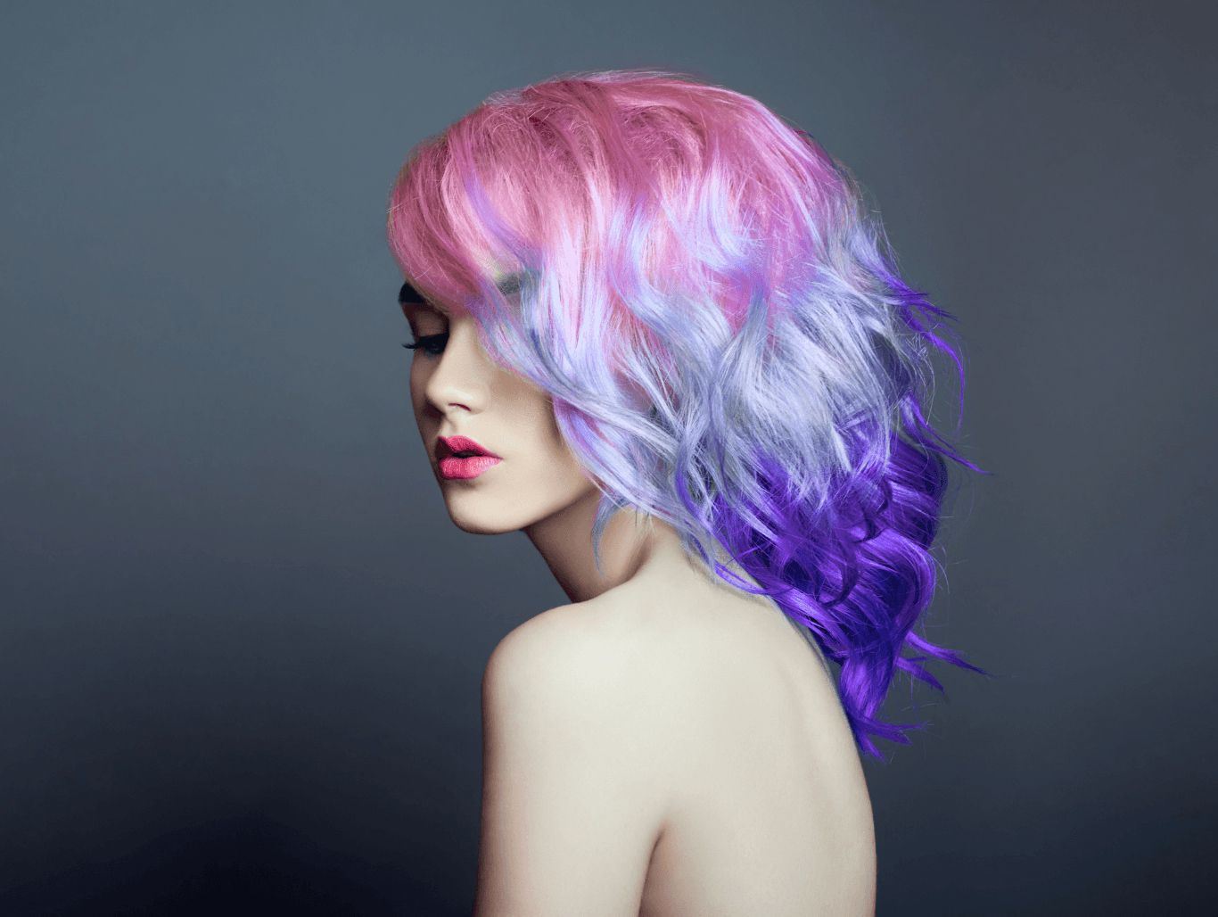 Woman with flowing pastel rainbow hair in pink, lavender, and violet tones, styled in loose waves — showcasing bold colour creativity and salon-quality finish by Changing Grooms, Weymouth.
