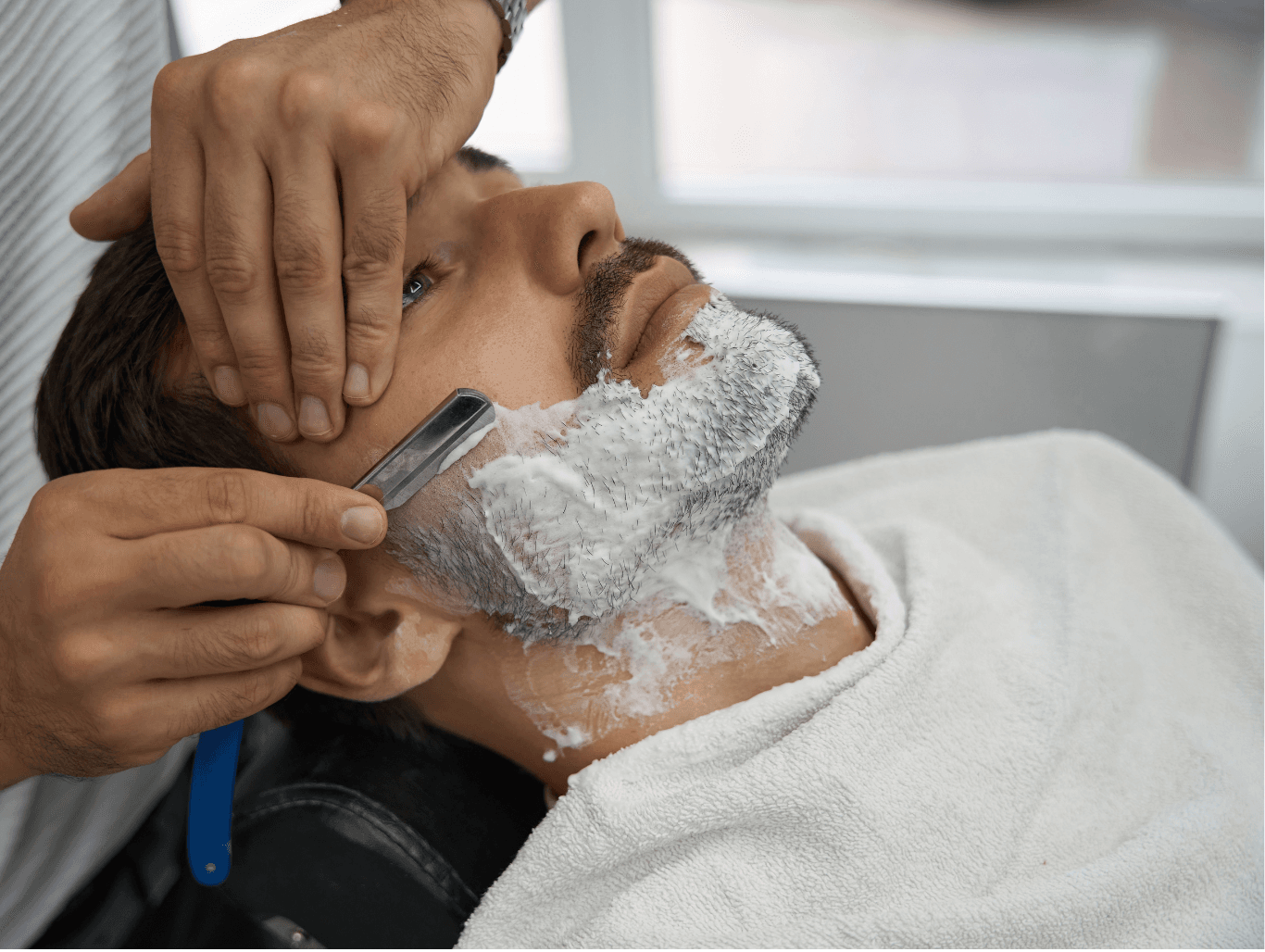 Barber performing a traditional cut-throat shave with foam and razor on a male client at a Weymouth barbershop