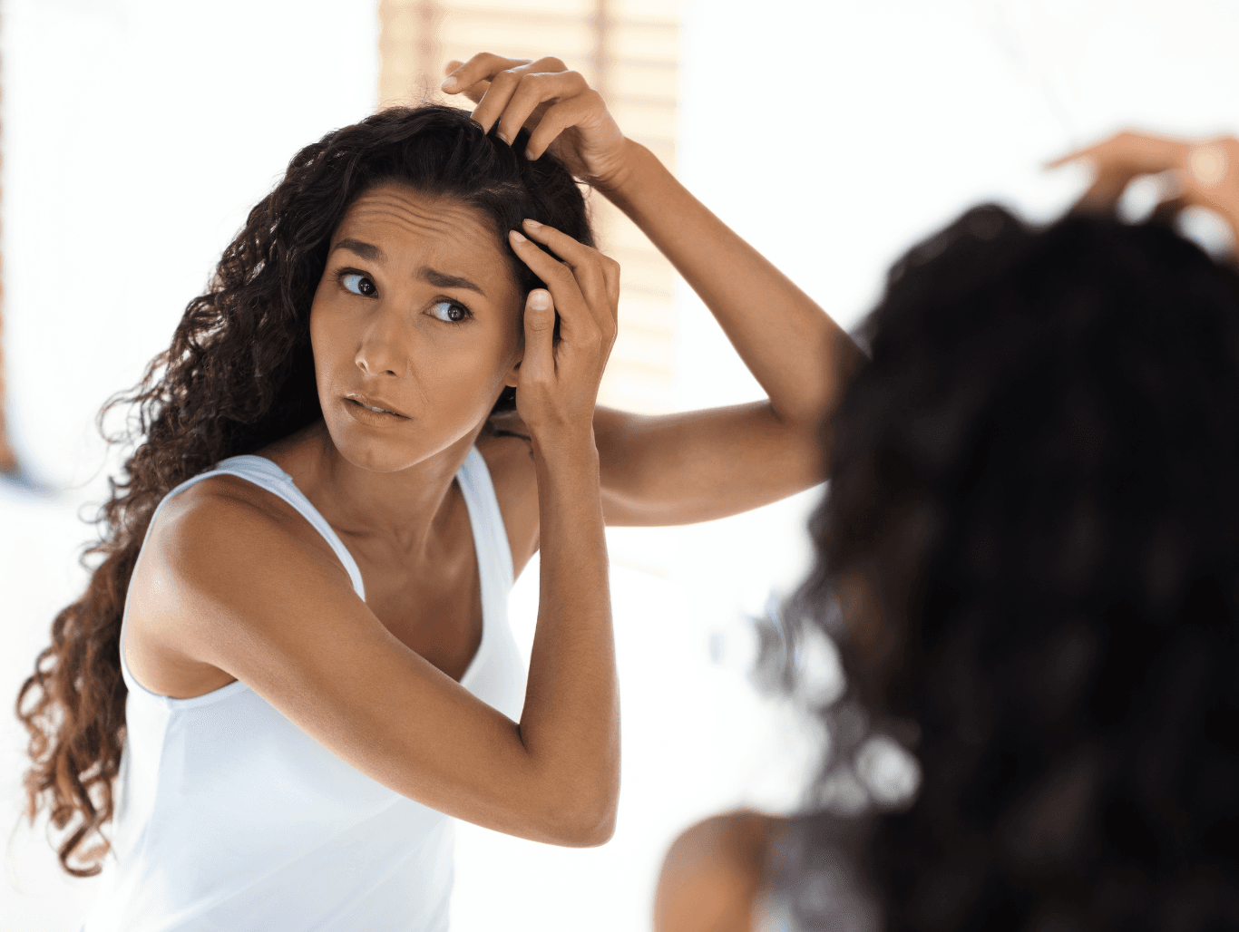 Concerned woman examining her scalp in the mirror before trichology consultation in Weymouth Dorset.